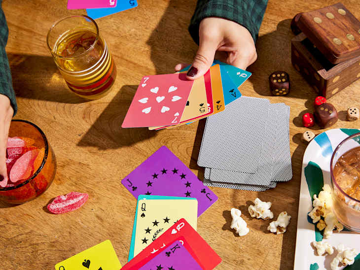 Hands of someone playing cards at table. The cards are bright and colorful. Snacks and other games on table