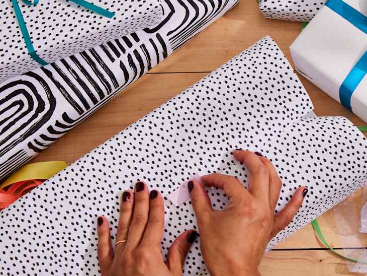 Hands wrapping gifts with black and white patterned paper on a wooden table.