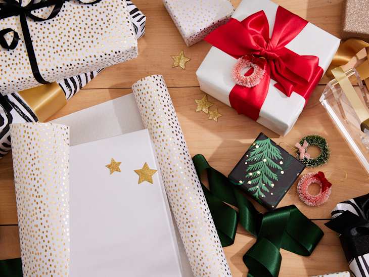 Gift wrapping scene with various wrapped presents, ribbons, and decorative items on a wooden surface.