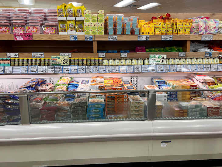 Frozen food display in a grocery store featuring various seafood, snacks, and packaged items on shelves above.