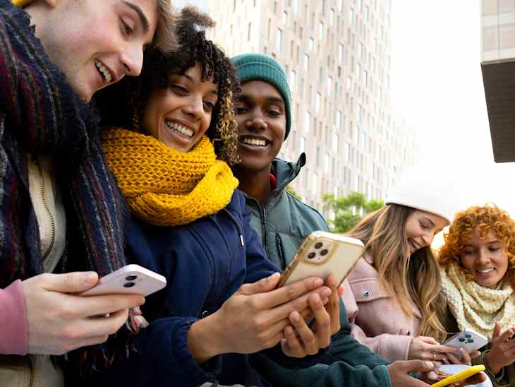 Young multiracial college student friends looking at mobile phones during winter day. Technology and lifestyle.