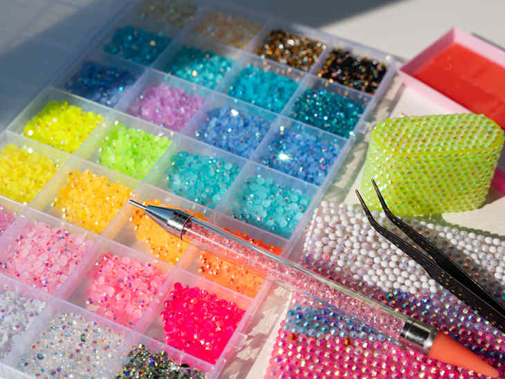 Bedazzling kit on a clean white background with colorful rhinestones, tweezers, embellished items, and a sparkling pink bedazzling pen. A trendy DIY craft setup for adding glamorous details to accessories and everyday objects