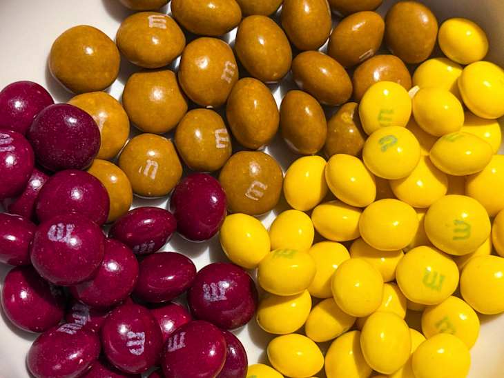 Three flavors of M&M's in a bowl cherry chocolate cupcake, lemon meringue pie, and peanut butter cinnamon roll.