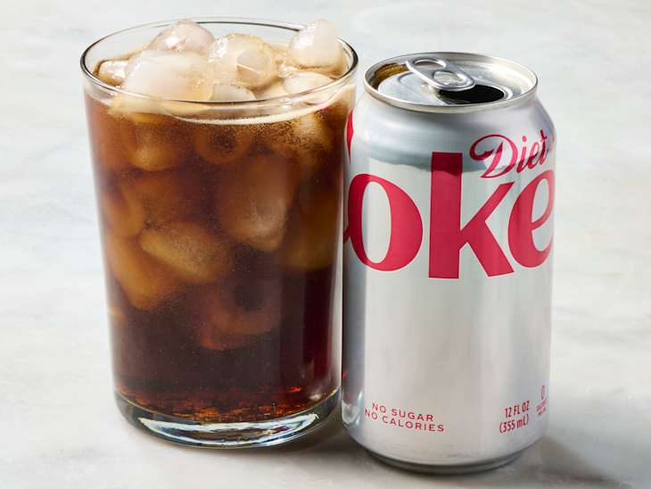 A glass filled with ice and dark soda next to a can of Diet Coke, both on a light surface.