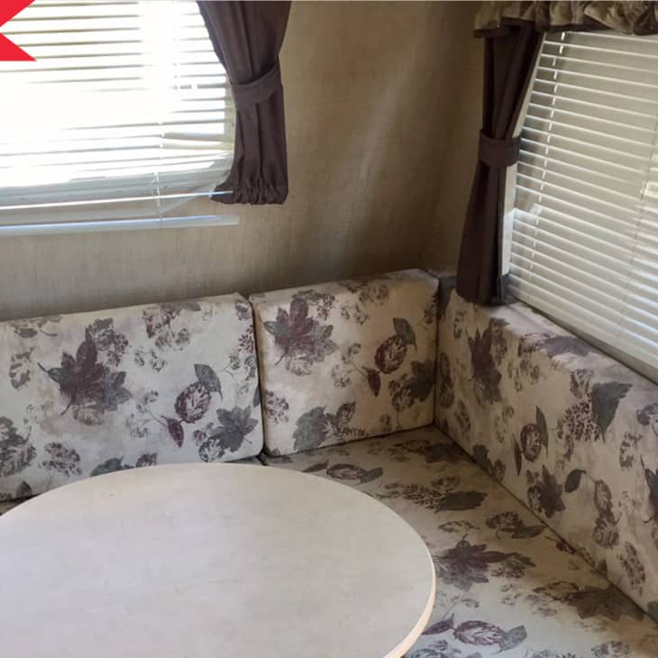Floral-patterned RV seating area with round table, brown curtains, and blinds.