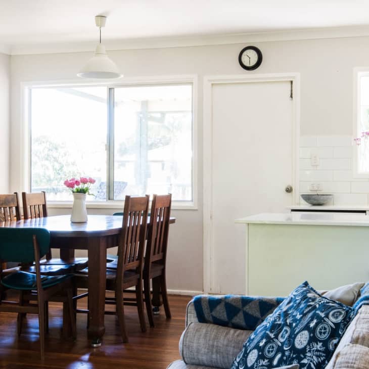 Dining room with wooden table and chairs, white shelves with dishes, and a vase of pink flowers.