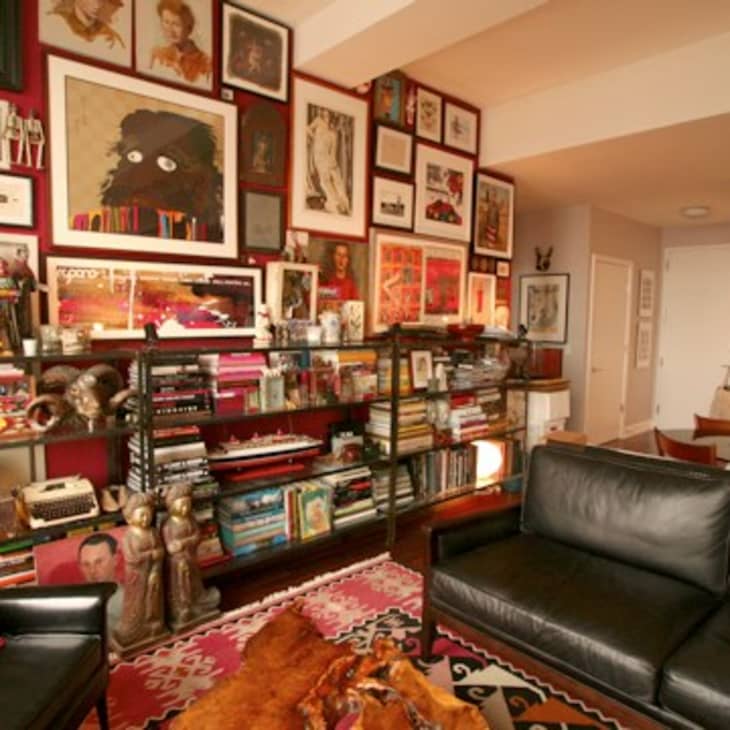 Eclectic living room with black leather sofas, colorful rug, and walls filled with framed art and bookshelves.