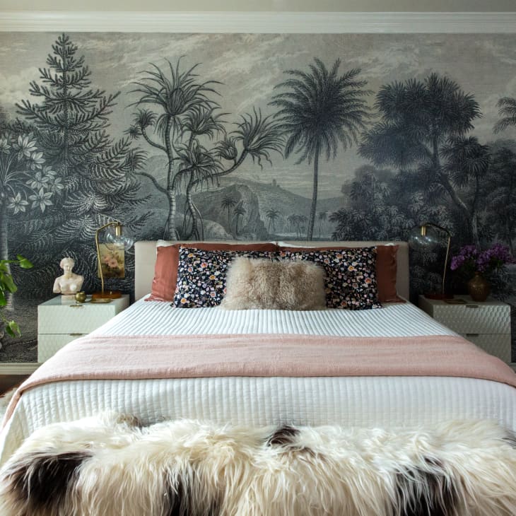 A bed in front of a wall with a mural of trees