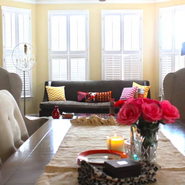Dining room with a dark sofa, colorful pillows, wooden table, pink roses, and candles.