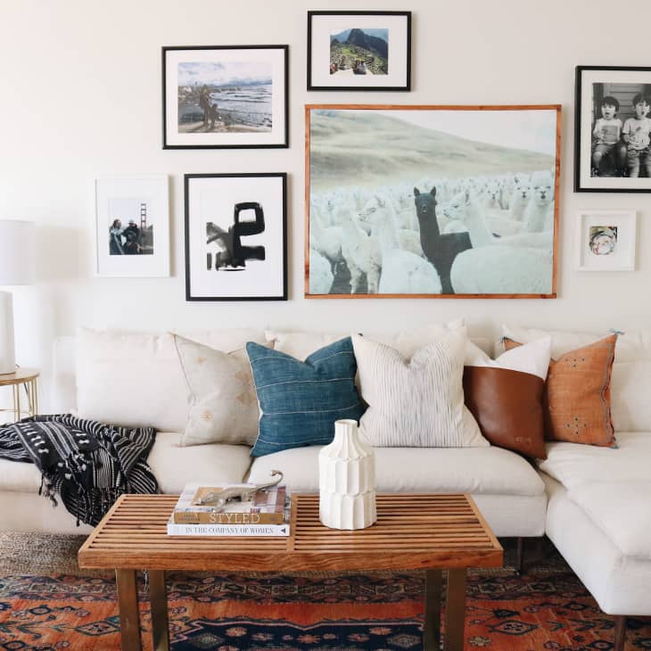 White sectional sofa with assorted pillows, wooden coffee table, and gallery wall in a cozy living room.