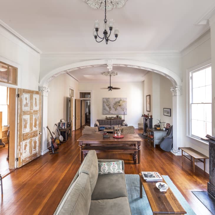 Spacious living room with arched entry, vintage fireplace, wooden floors, and eclectic decor, including a large wall map.