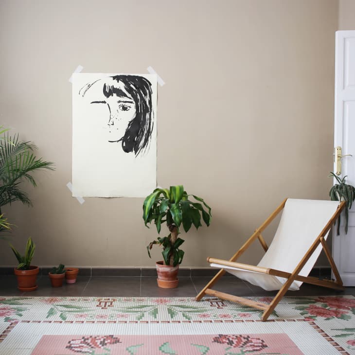 Room with a canvas chair, potted plants, and a wall art portrait on a beige wall.