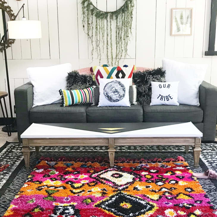 Gray sofa with colorful pillows, vibrant patterned rug, and wall decor in a cozy living room setting.