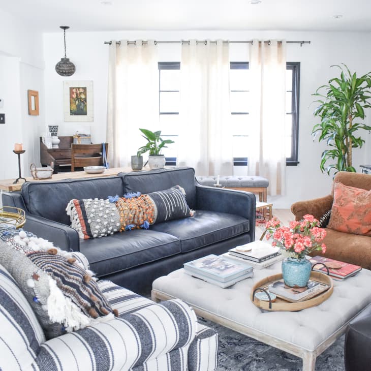 Living room with a navy sofa, striped armchair, brown chair, coffee table, plants, and colorful cushions.