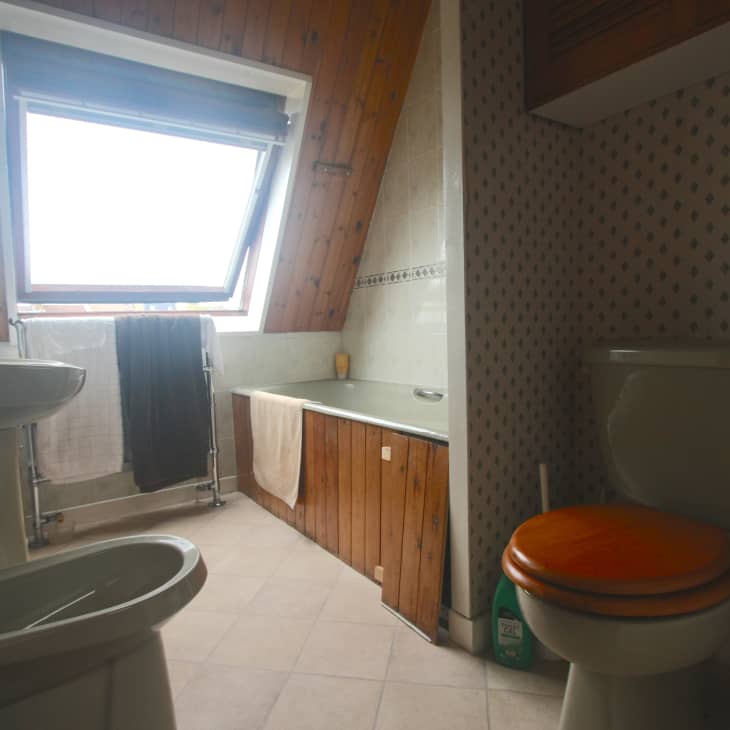 Attic bathroom with sloped ceiling, wooden paneling, bathtub, sink, and toilet with orange seat.
