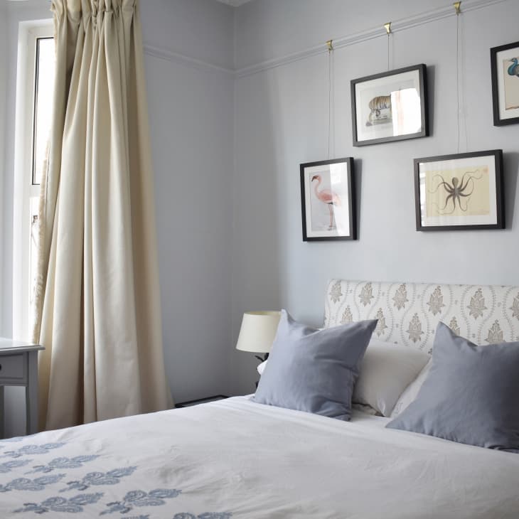 Bedroom with patterned headboard, blue pillows, framed animal art, and a small desk with a chair by the window.