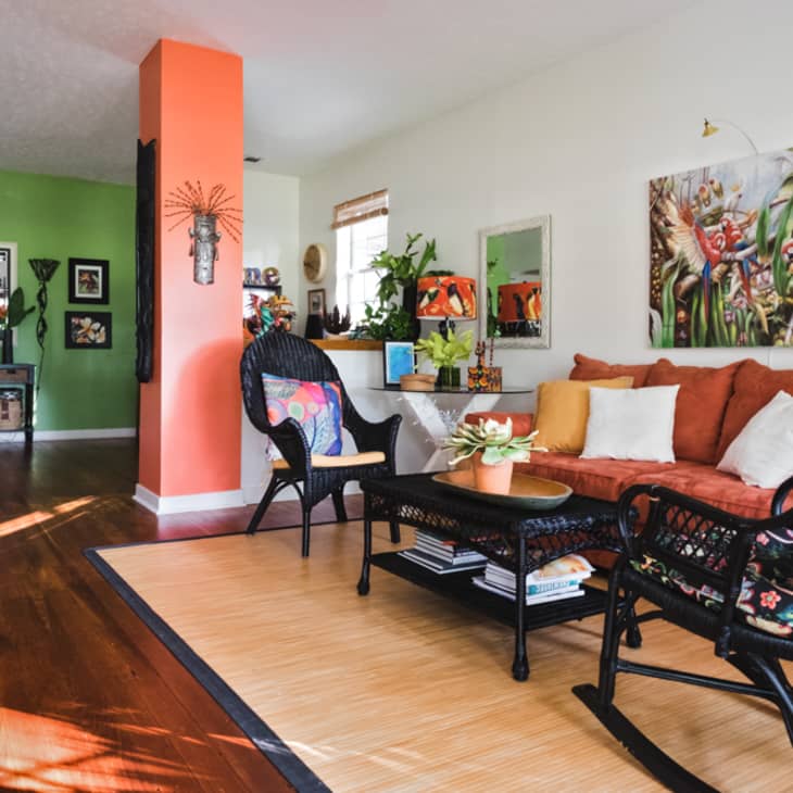 Living room with orange sofa, colorful pillows, wicker chairs, parrot artwork, and green accent wall with decor.
