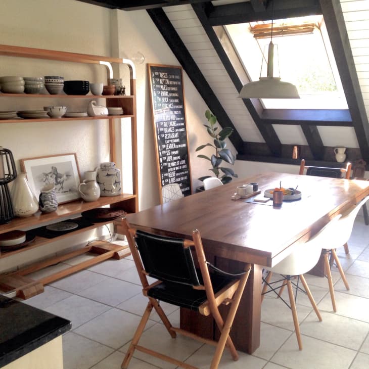 Dining room with wooden table, black and white chairs, open shelving with ceramics, and a slanted skylight.