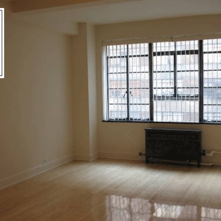 Empty room with large grid windows, beige walls, and a dark radiator under the window.