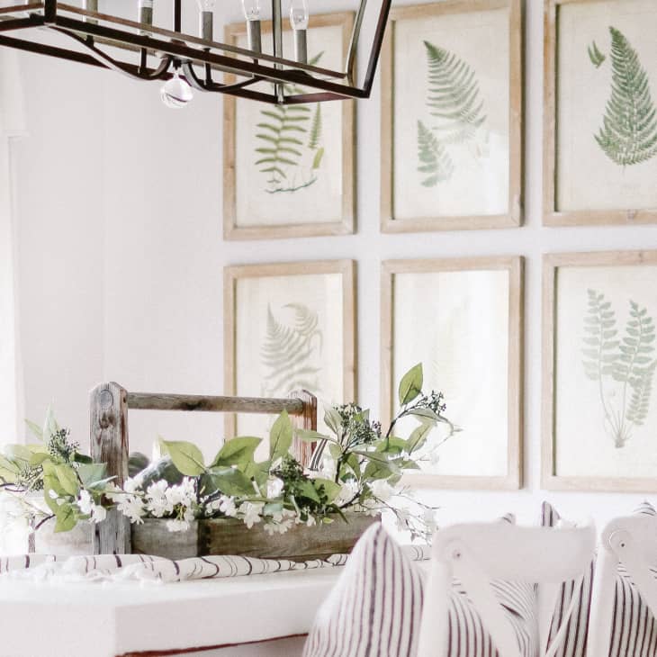 Dining room with a rustic centerpiece, striped cushions, and six framed fern prints on the wall.