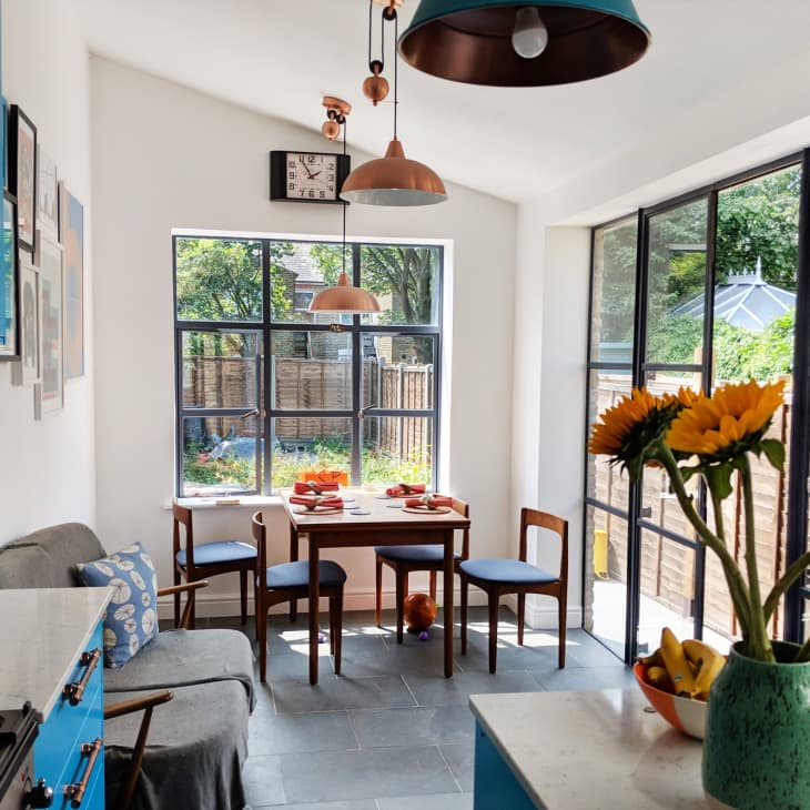 Bright kitchen with blue cabinets, sunflowers in a vase, and a dining table set for four near large windows.