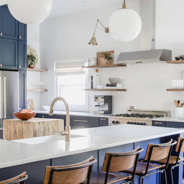 Modern kitchen with navy cabinets, white countertops, stainless steel appliances, and wooden shelves with decor items.