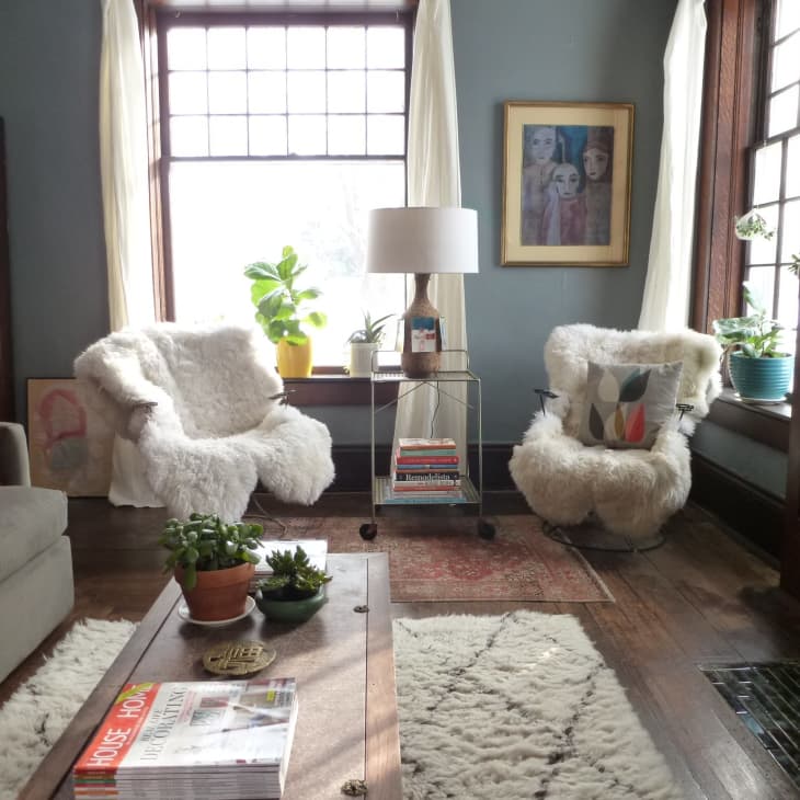 Cozy living room with fluffy armchairs, a gray sofa, plants, and a coffee table with magazines.
