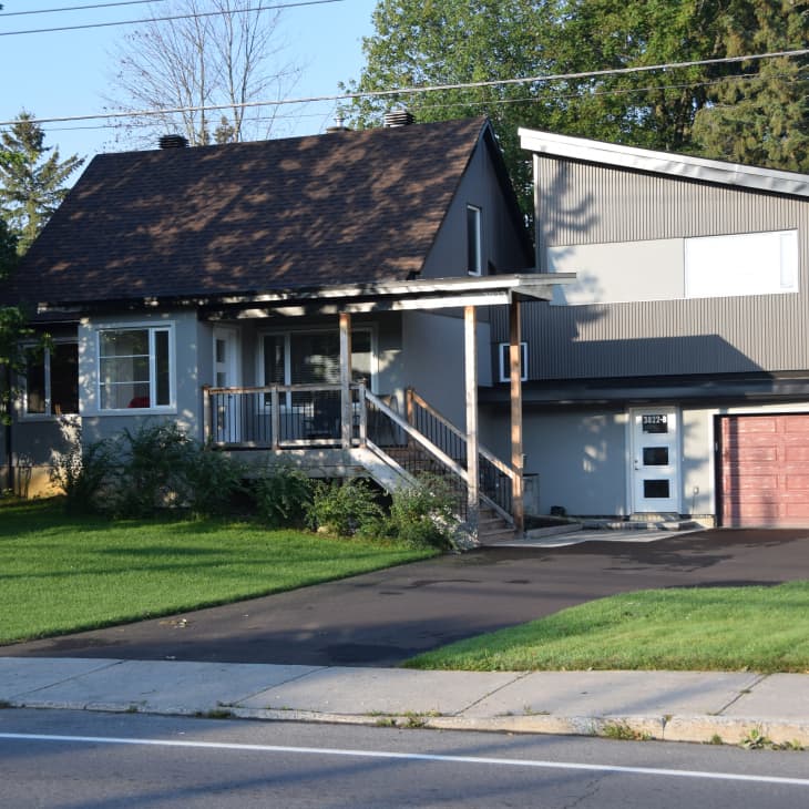 Gray house with a sloped roof, front porch, and attached garage, surrounded by green lawn and trees.