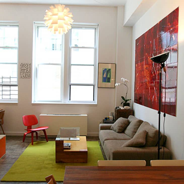 Modern living room with gray sofa, red chair, green rug, and large abstract red artwork on the wall.
