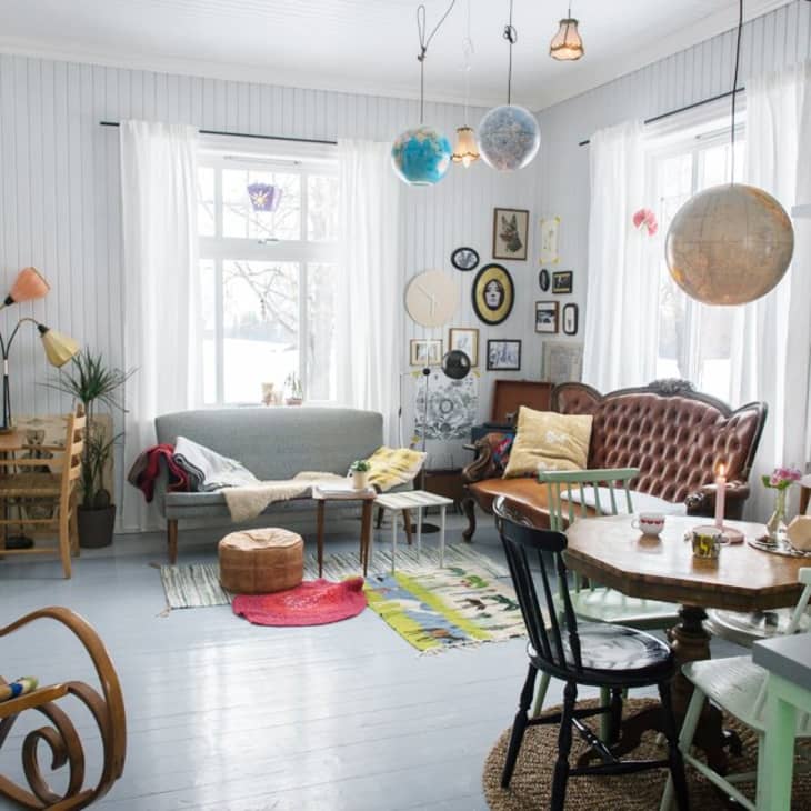 Eclectic living room with vintage furniture, globe lights, wall art, and a mix of colorful rugs and cushions.