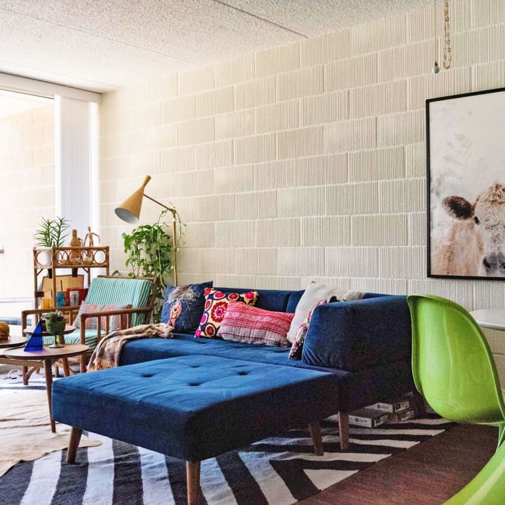 Living room with blue sectional sofa, colorful pillows, green chair, cow artwork, and sliding glass doors to a balcony.