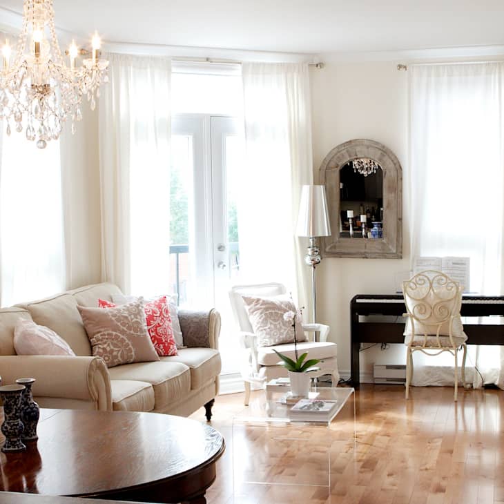Elegant living room with chandelier, beige sofa, red pillows, piano, and ornate mirror.