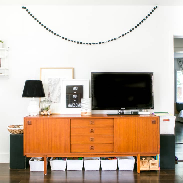 Mid-century modern console with TV, black lamp, framed art, and decorative items, flanked by shelves and doorway to bedroom.