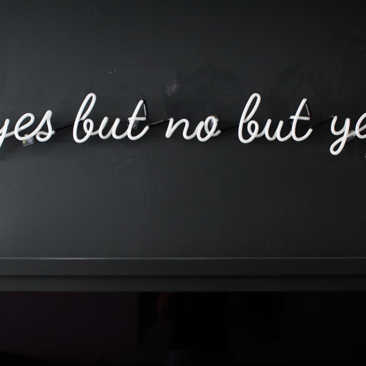 Neon sign reading "yes but no but yes" on a dark wall.