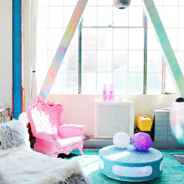 Colorful room with a pink throne chair, fluffy sofa, iridescent egg chair, and a round table with decorative spheres.