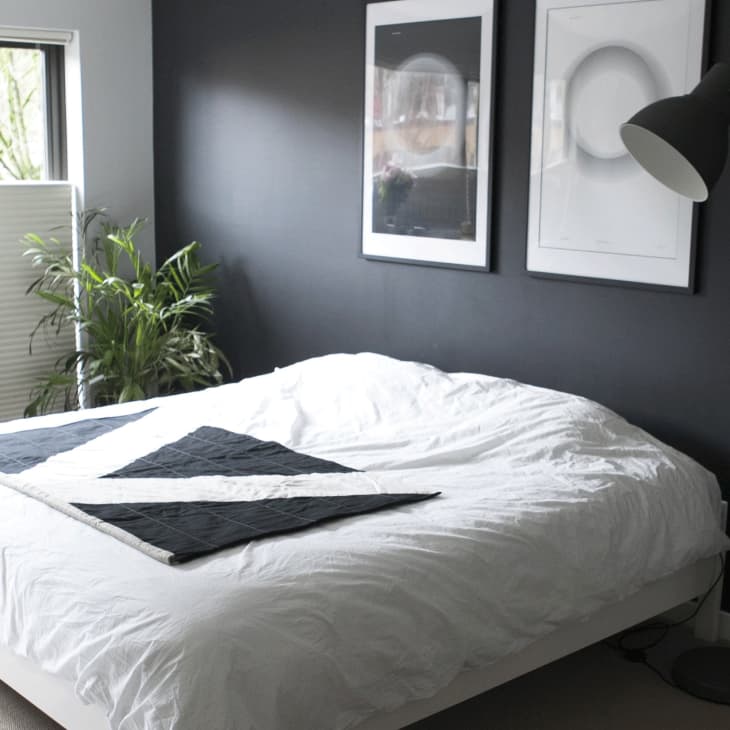 A white bed with a black blanket showing a V in front of a black wall with black and white pictures.