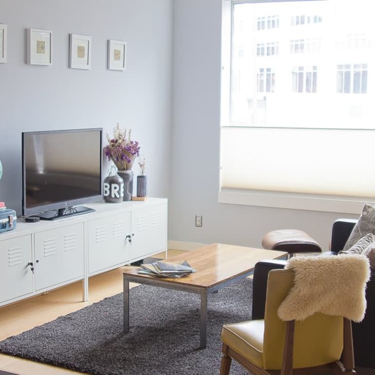 Modern living room with black sofa, white TV stand, globe, books, and a wooden coffee table on a gray rug.