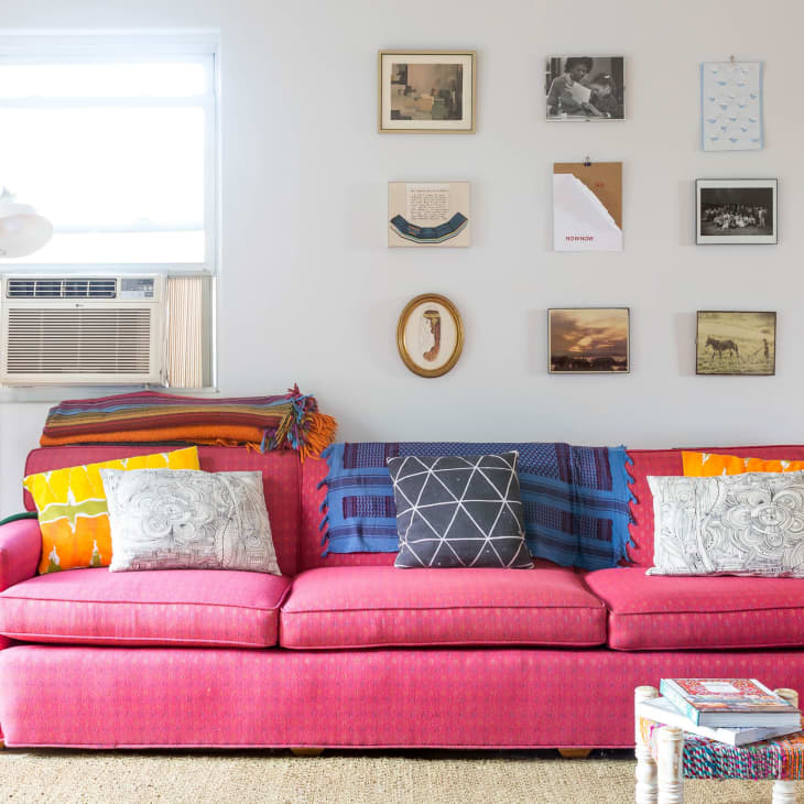 Pink sofa with colorful cushions, wall art, guitar, and air conditioner in a cozy living room.