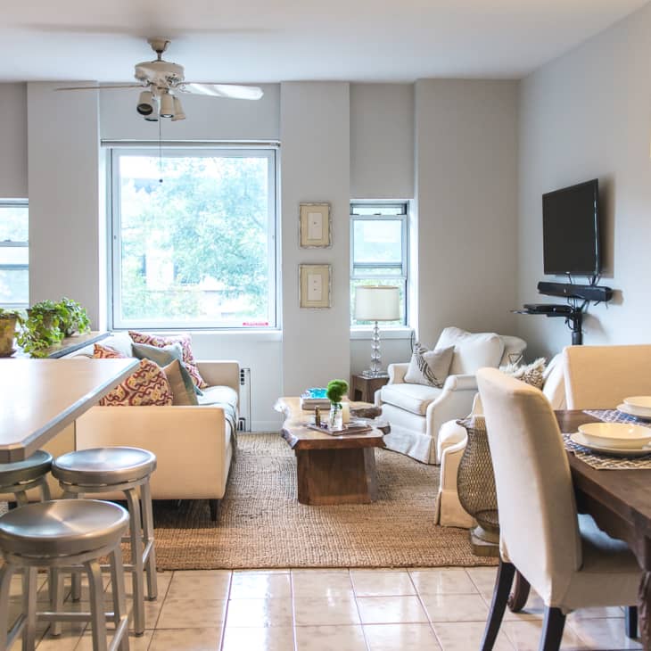 Open-plan living and dining area with a white sofa, wooden dining table, bar stools, and wall-mounted TV.