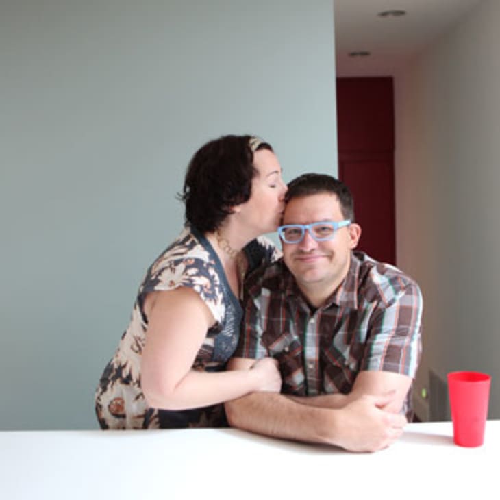 Woman kissing man on the cheek in a modern room with a red cup on the table.