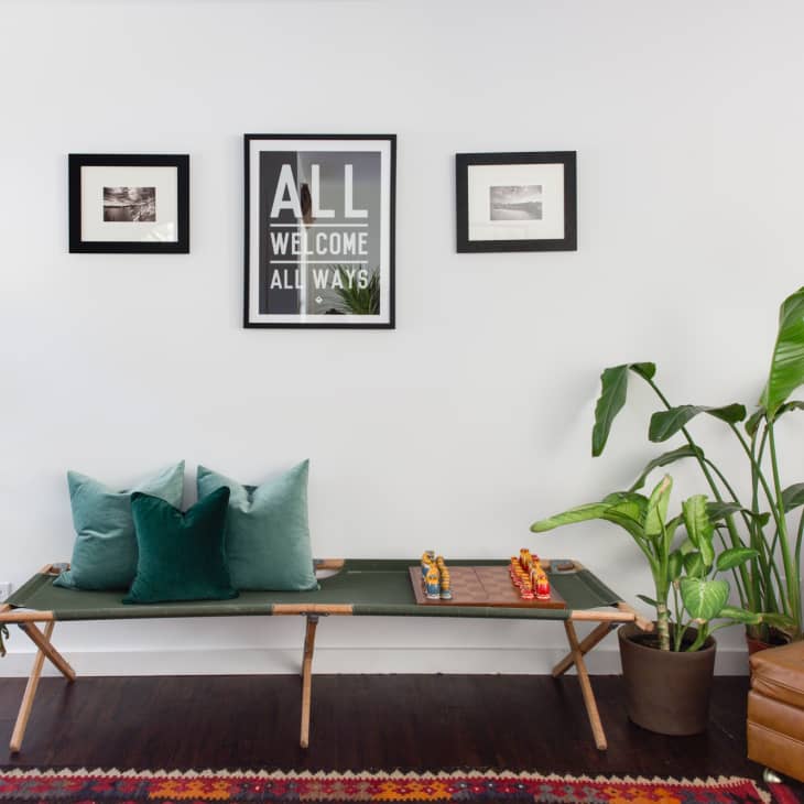 Living room with green bench, colorful pillows, chess set, framed art, and potted plants on dark wood floor.