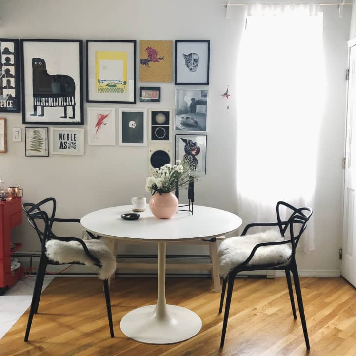 Dining area with round white table, black chairs with fur cushions, red cart, and eclectic wall art gallery.