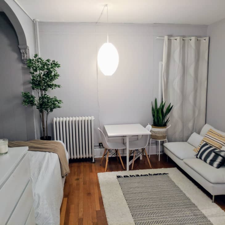 Cozy living room with a white sofa, small dining table, potted plants, and a patterned rug on wooden flooring.