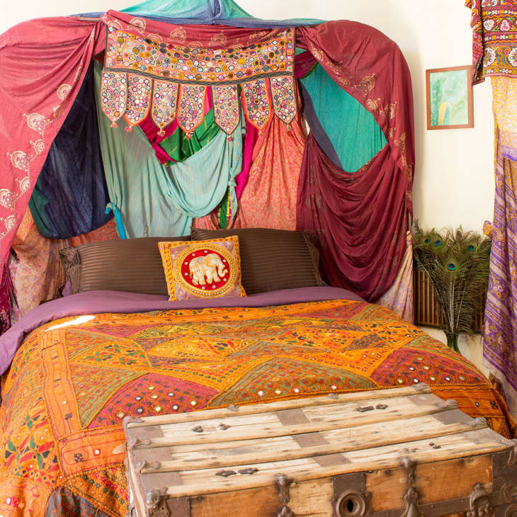 Bohemian bedroom with colorful canopy, elephant pillow, ornate bedspread, and wooden chest at the foot of the bed.
