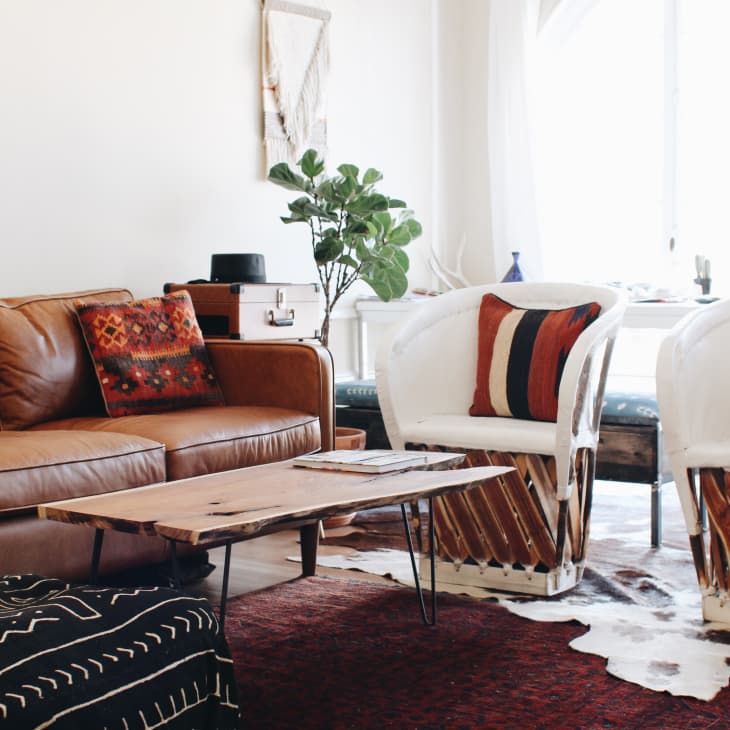 Living room with brown leather sofa, wooden coffee table, white chairs with red patterned cushions, and a potted plant.