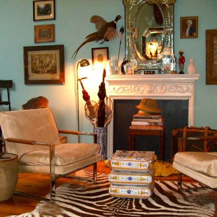 Eclectic living room with vintage armchairs, zebra rug, ornate mirror, and framed art on blue walls.