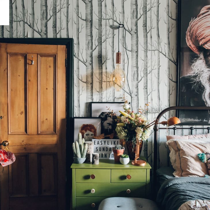 Bedroom with tree-patterned wallpaper, wooden door, green dresser, and large portrait of a man in a turban.