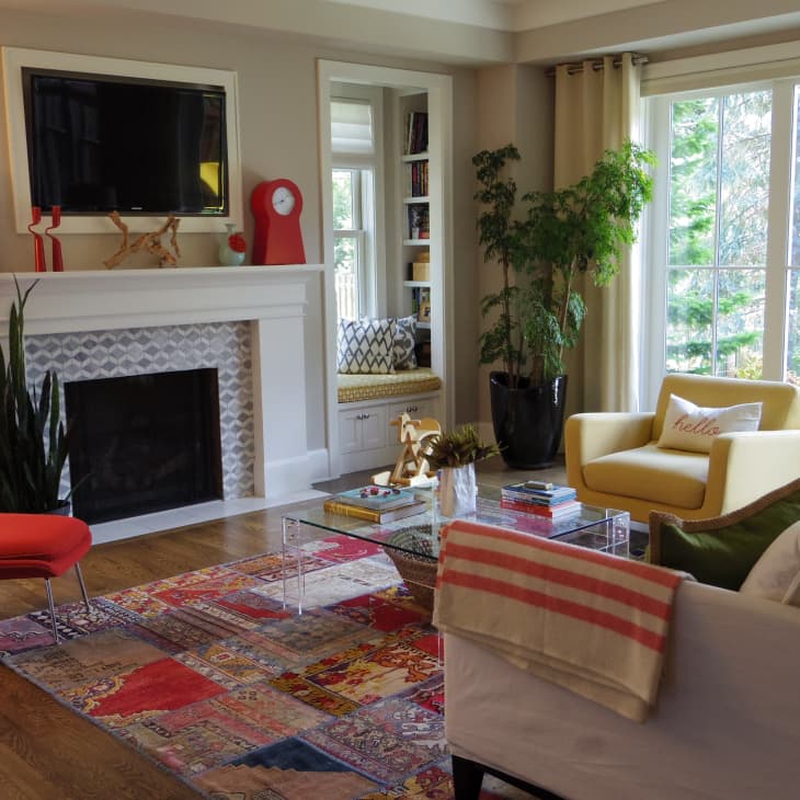 Living room with a fireplace, red and yellow chairs, colorful rug, and large window with garden view.