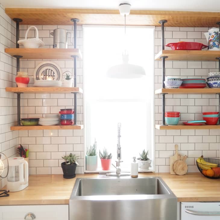 Kitchen with open shelves, colorful dishes, wooden countertops, white subway tiles, and potted plants by the sink.