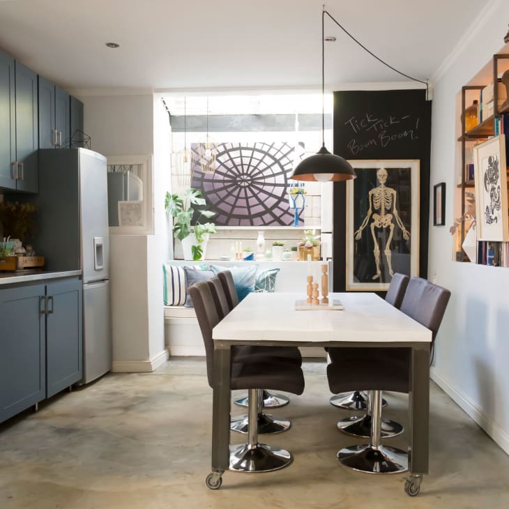 Modern kitchen with blue cabinets, stainless steel appliances, a white dining table, black chairs, and eclectic wall decor.